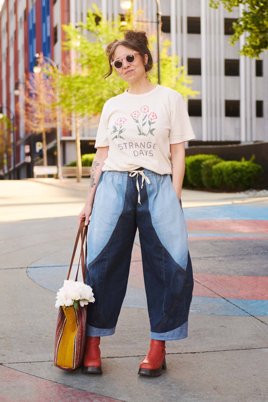 Woman wearing a graphic t-shirt and denim pants with a colorful bag, standing on a city street.