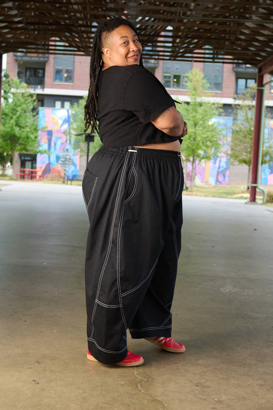 Person wearing a black outfit with red shoes standing in an outdoor setting.