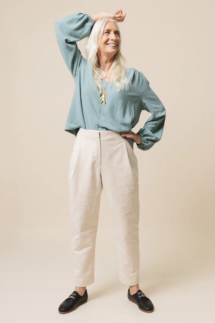 Woman wearing a light blue blouse and beige pants against a beige background