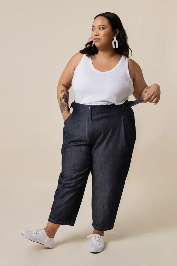 Woman wearing a white tank top and dark jeans against a beige background