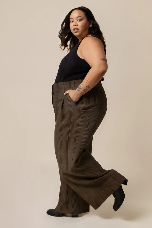 Woman wearing brown wide-leg pants and a black top on a beige background