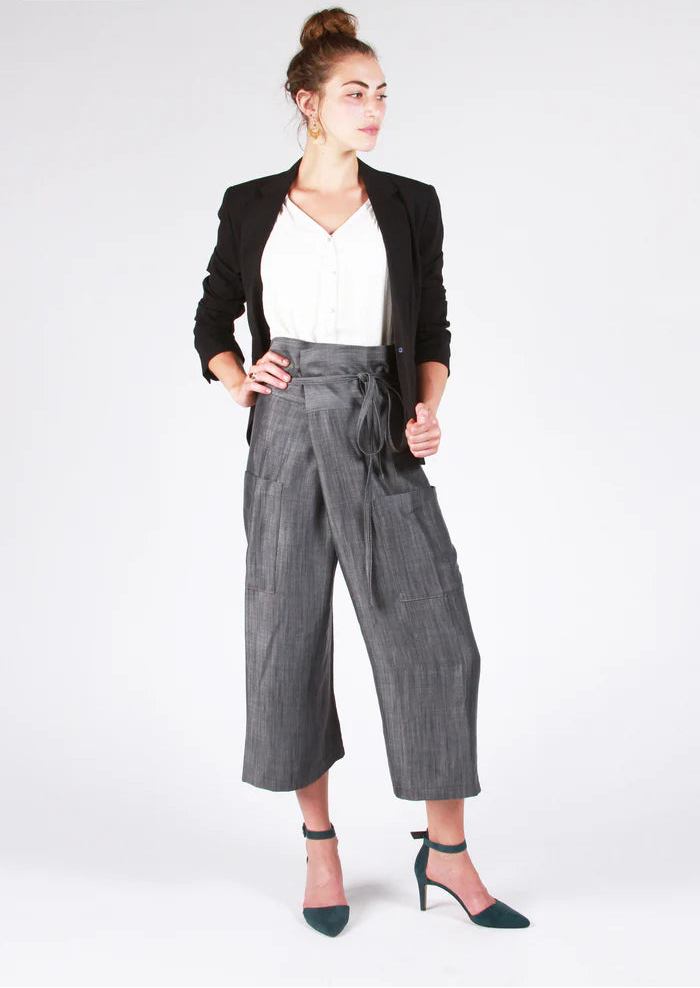 Woman wearing a black blazer, white top, and gray pants on a white background