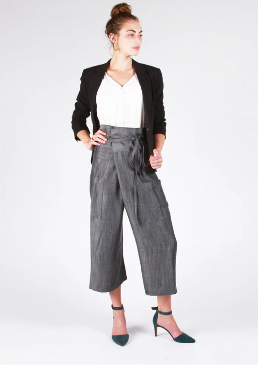 Woman wearing a black blazer, white top, and gray pants on a white background