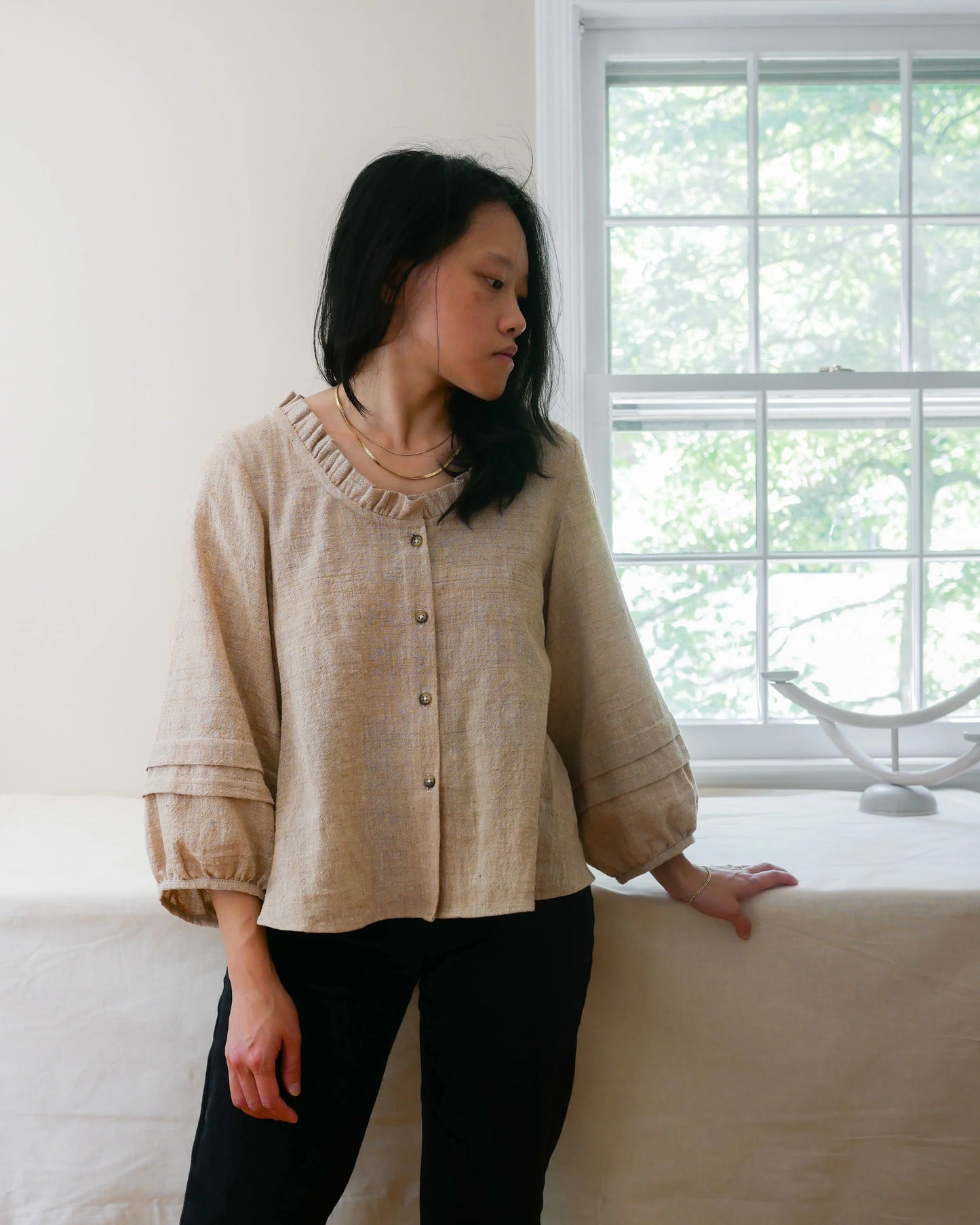 Woman wearing a beige blouse standing in a room with a window in the background
