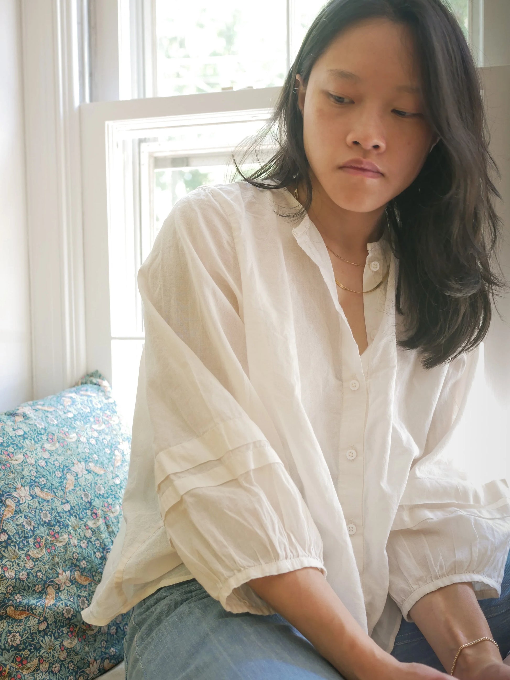 Woman wearing a white blouse sitting on a floral couch.