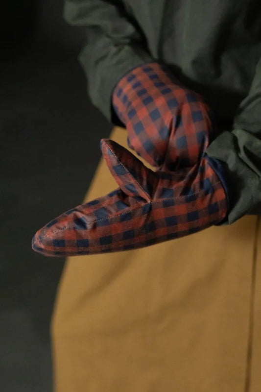 Red and blue plaid mittens worn by a person in a dark jacket and brown pants.