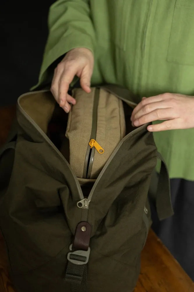 Person opening a green backpack with a brown interior pocket.