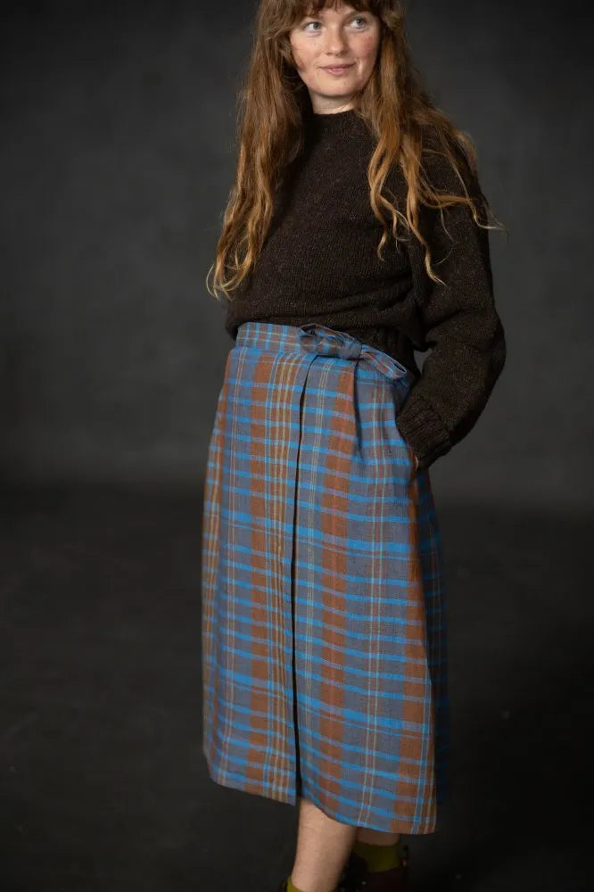 Woman wearing a brown sweater and blue plaid skirt against a dark background