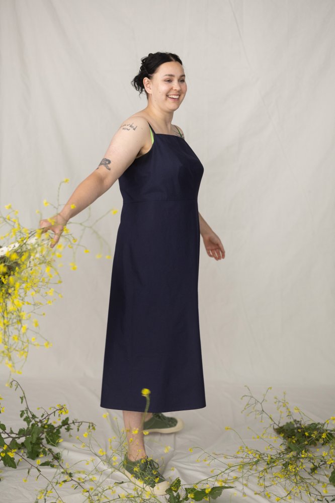 Woman in a navy dress standing among yellow flowers on a plain background