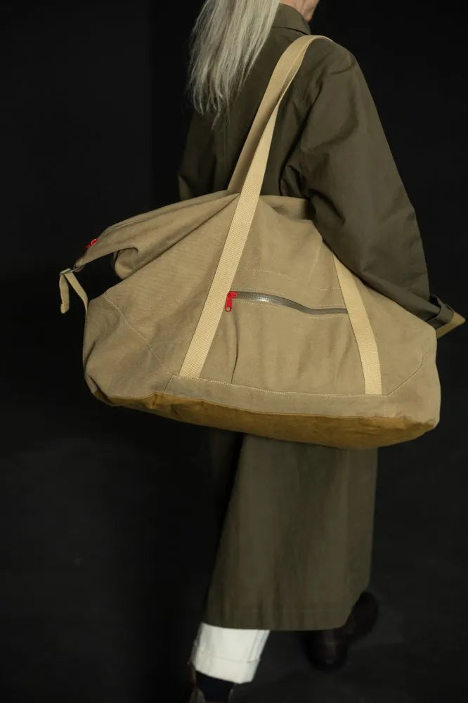 Person wearing a large brown bag with beige straps on a dark background