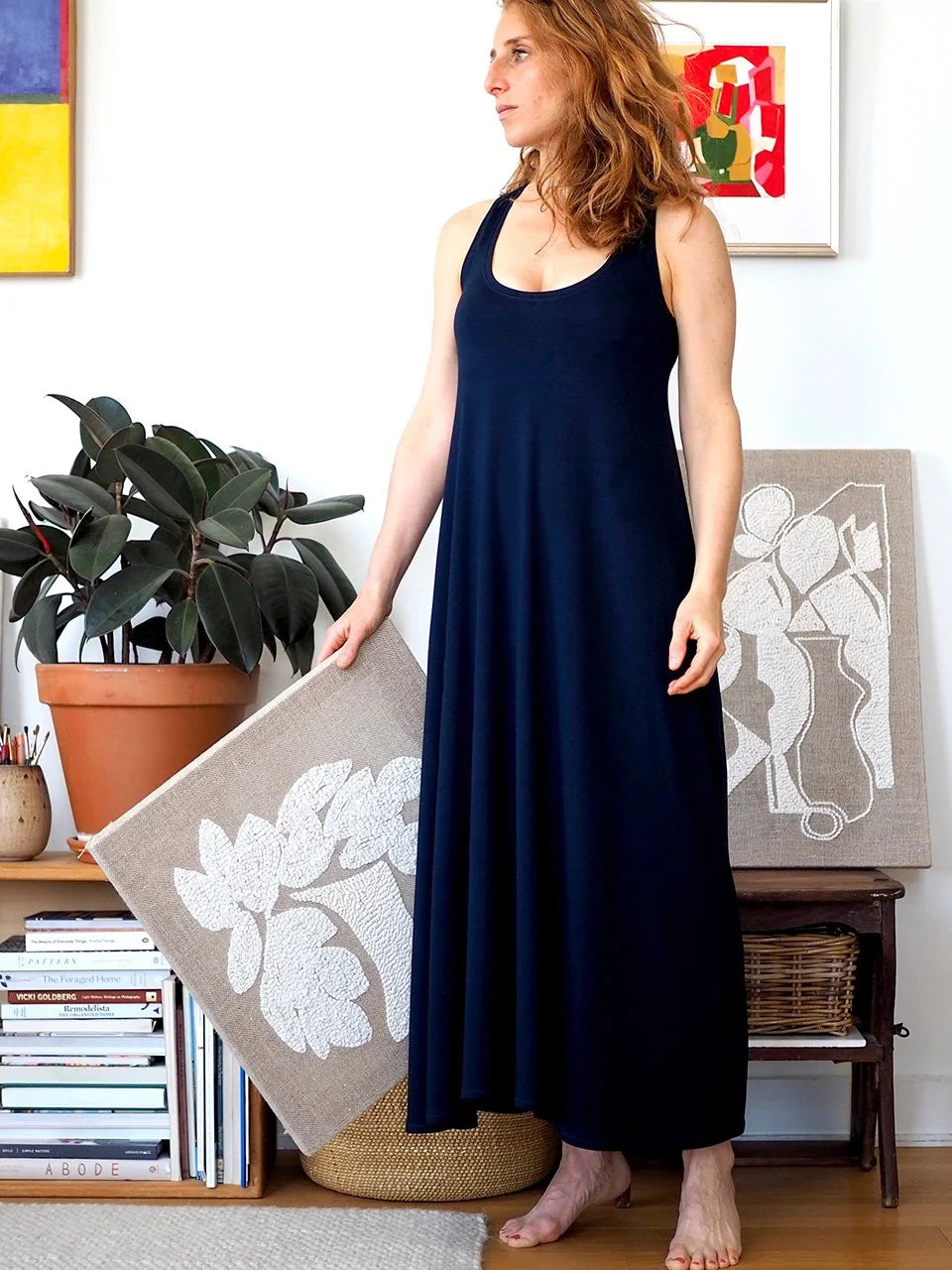 Woman wearing a navy blue dress standing in a room with books and decorative items.