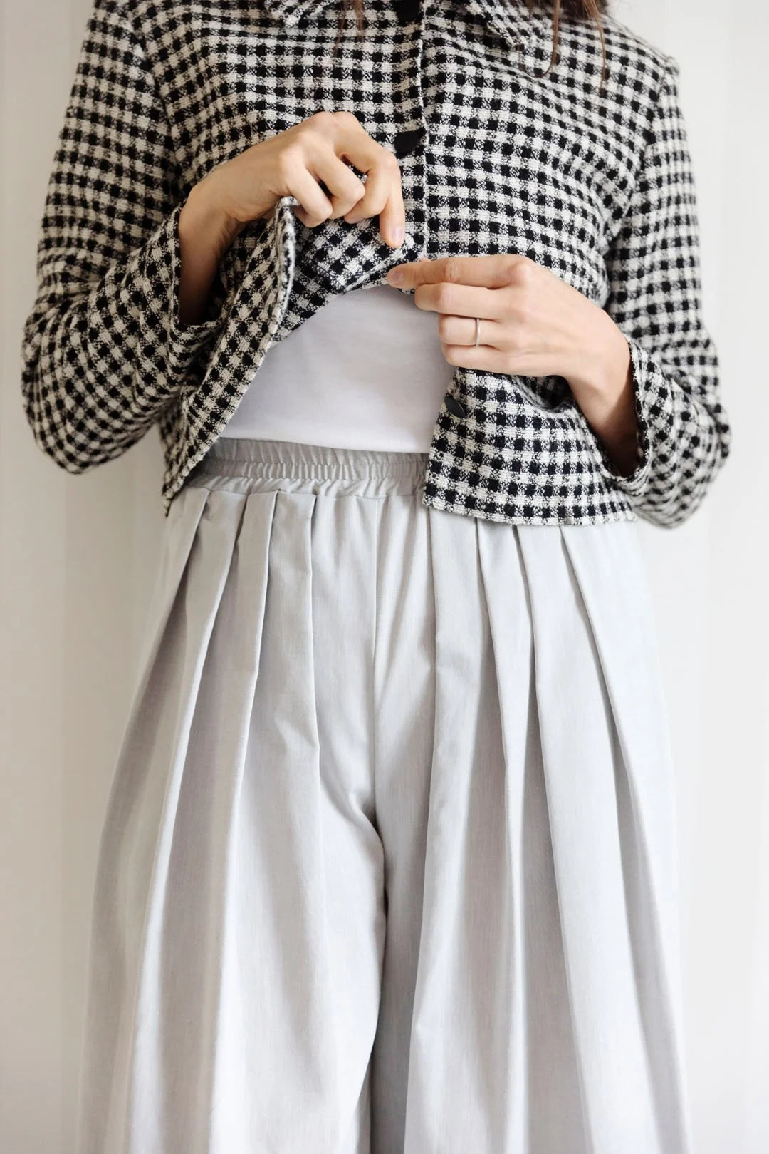 Person wearing a black and white checkered jacket with light-colored pants on a plain background