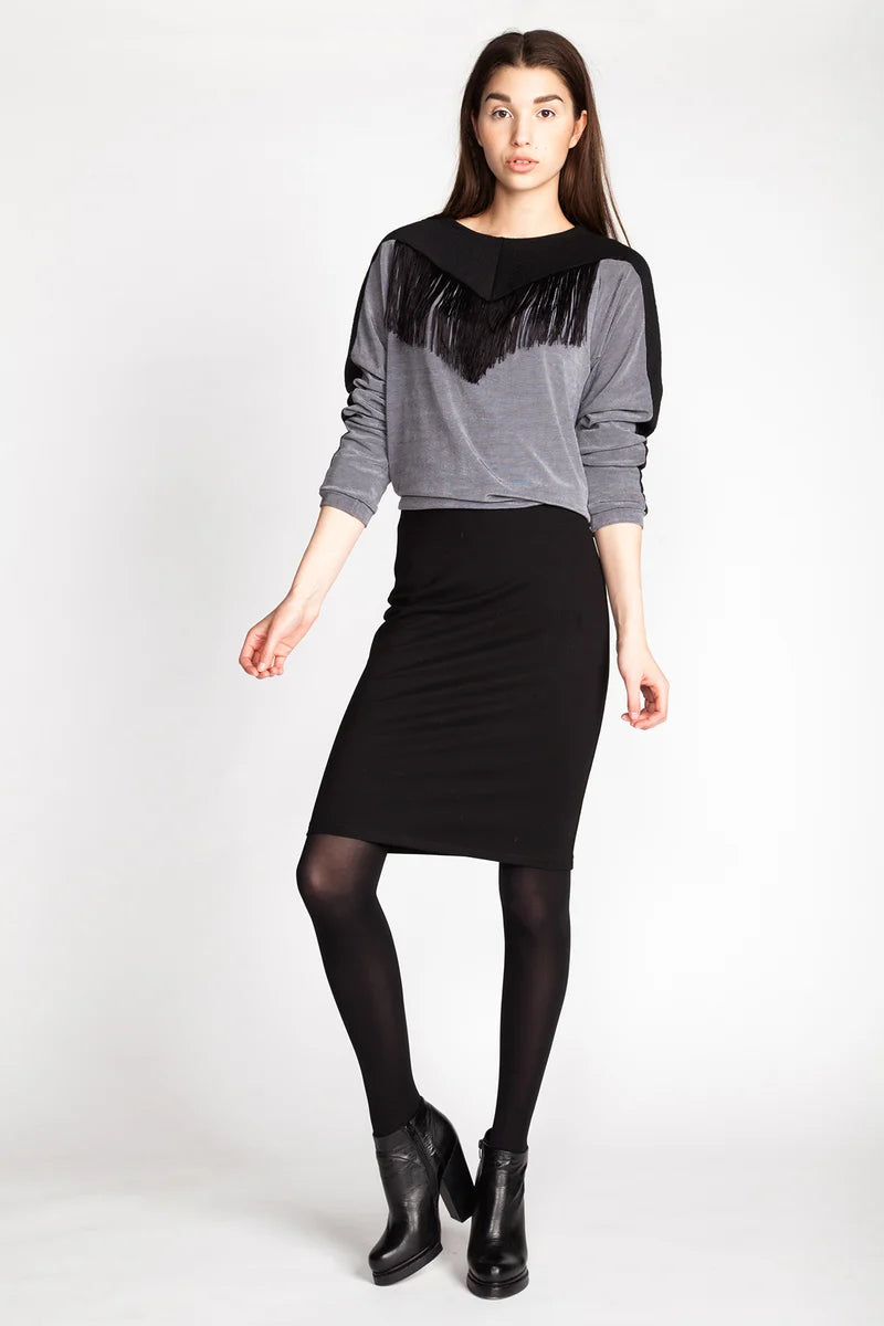 Woman wearing a gray sweater with black fringe details and a black skirt on a white background