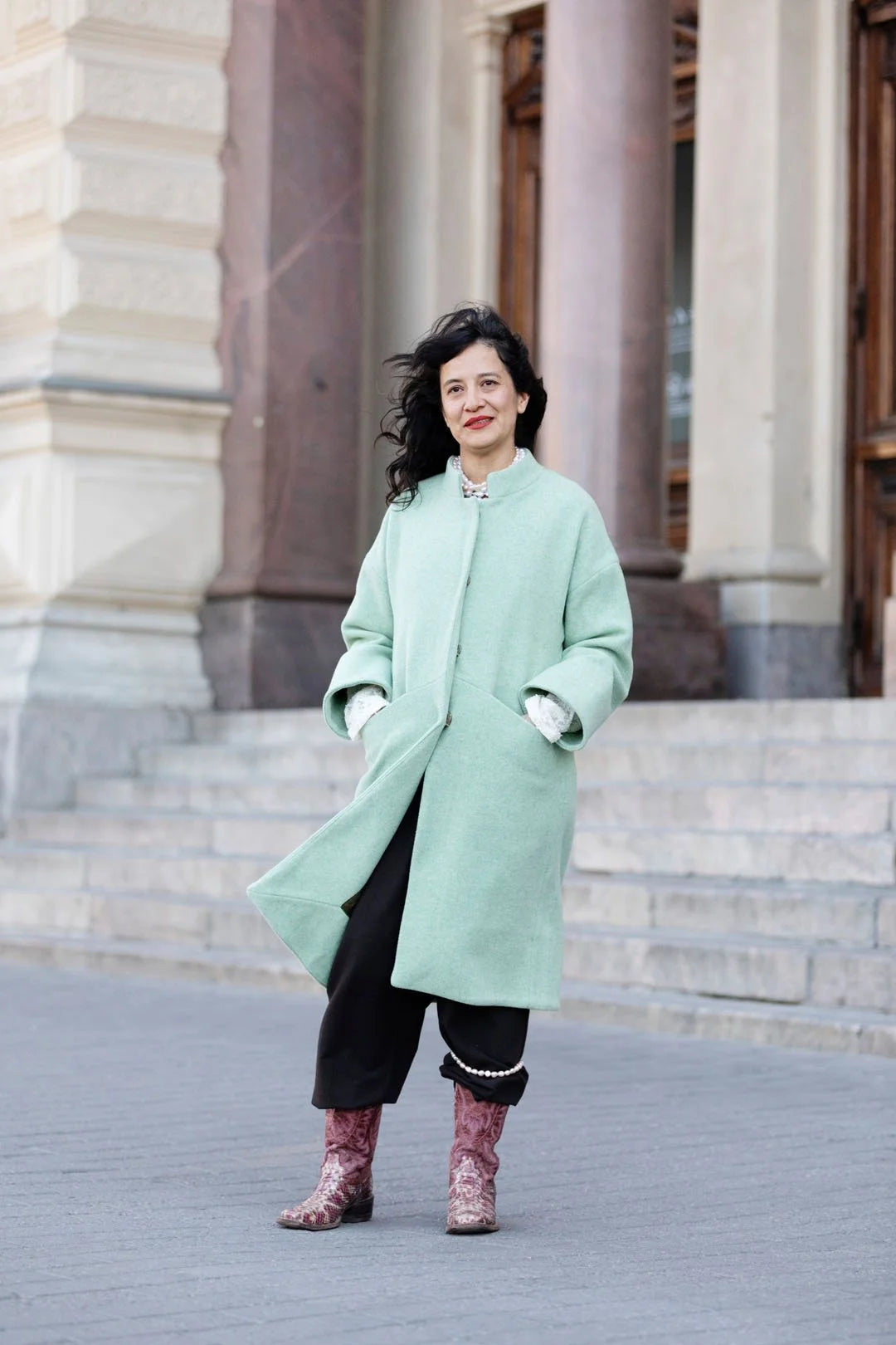 Woman in a light green coat standing on steps in front of a building