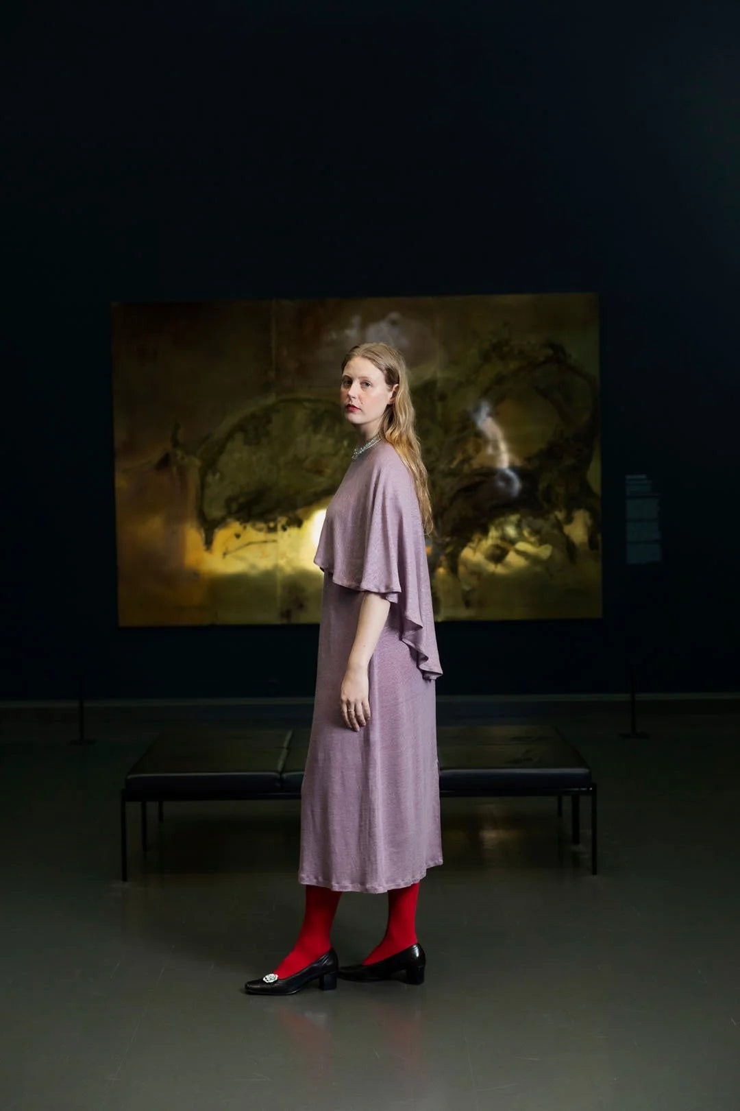 Woman in a purple dress standing in front of a large painting in a dark room