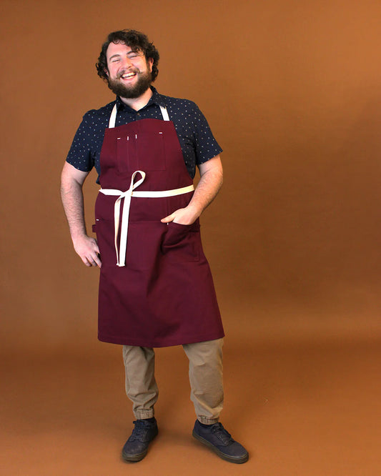 Man wearing a maroon apron with a white strap on a brown background