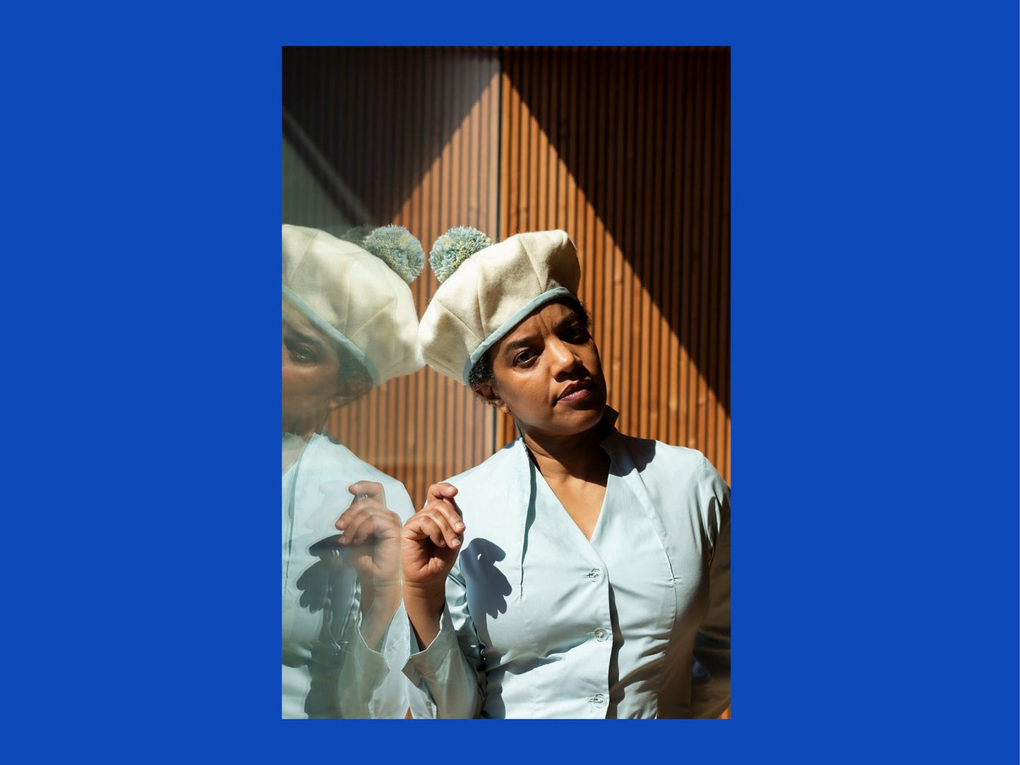 Woman wearing a white outfit and hat in front of a mirror with a blue border