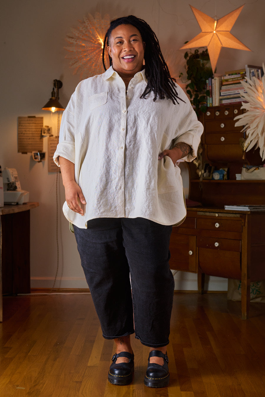 Person wearing a white textured shirt and dark pants in a room with wooden floors and furniture.
