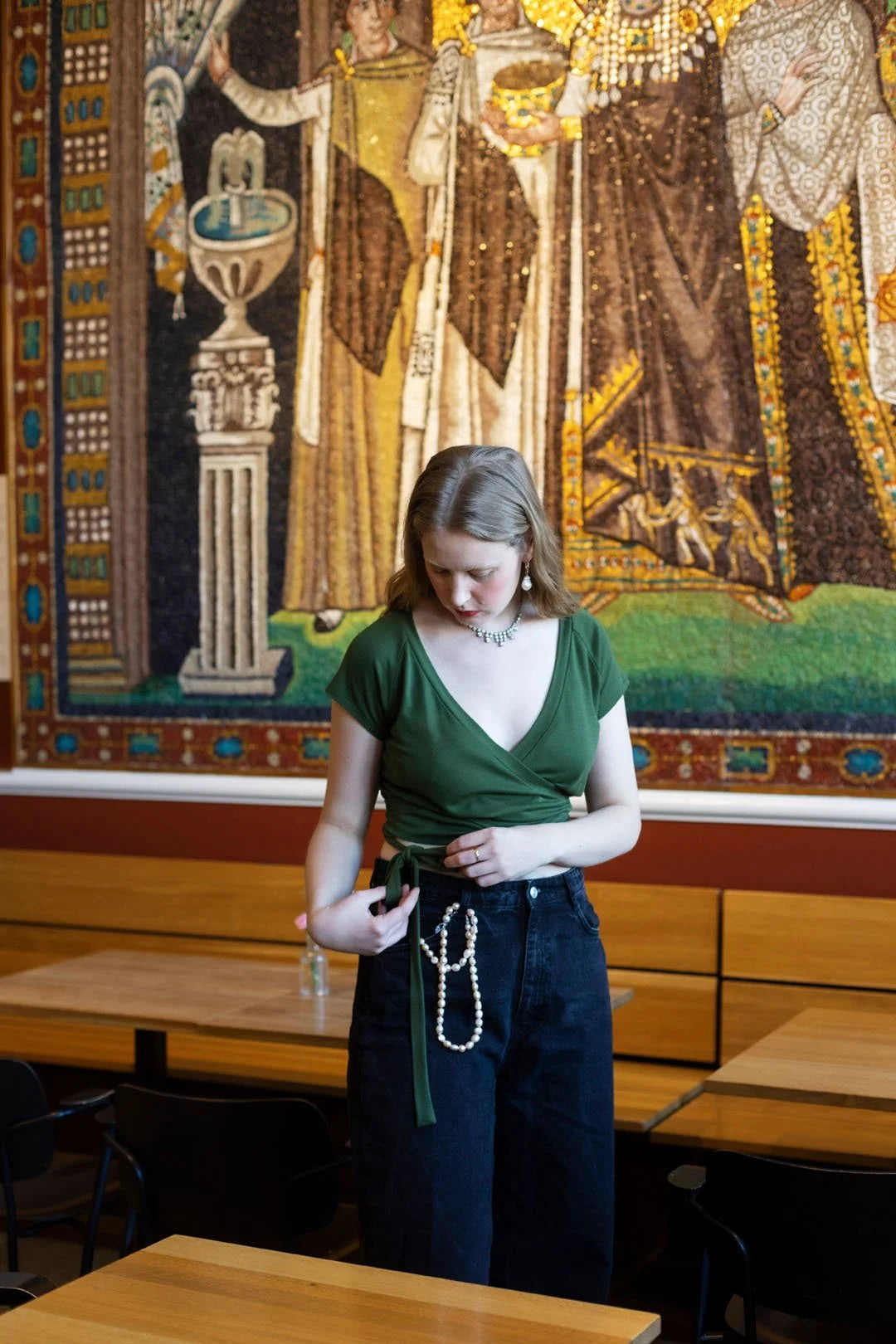 Woman in a green shirt and blue jeans standing in front of a large tapestry.