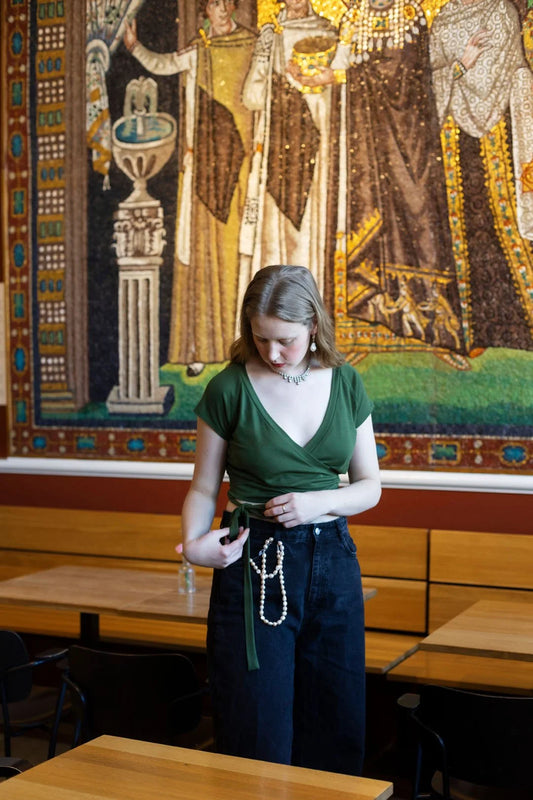 Woman in a green shirt and blue jeans standing in front of a large tapestry.