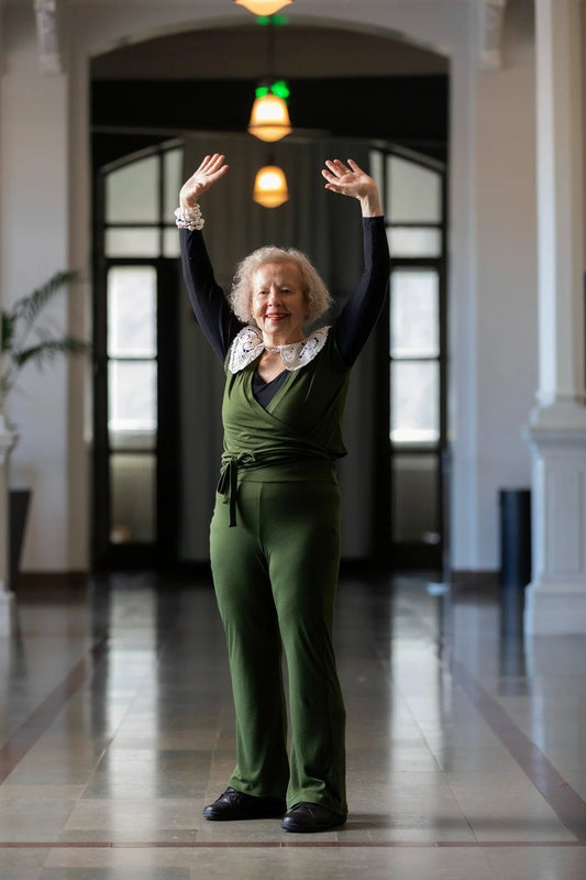 Woman in a green jumpsuit standing in a hallway with arms raised