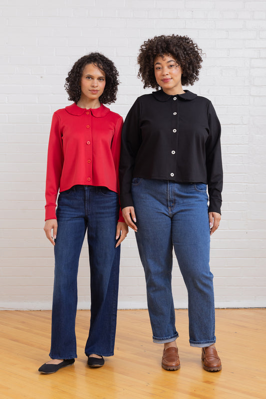 Two people wearing red and black button-up shirts with blue jeans against a white wall.