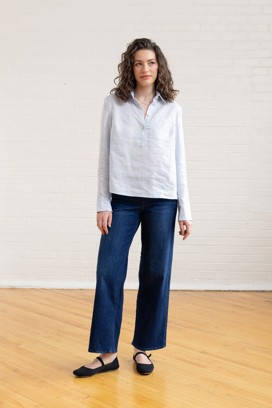 Woman wearing a white shirt and blue pants standing on a wooden floor with a white wall background