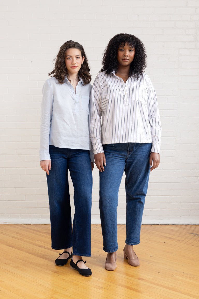 Two women wearing matching outfits of striped shirts and jeans standing against a white wall.