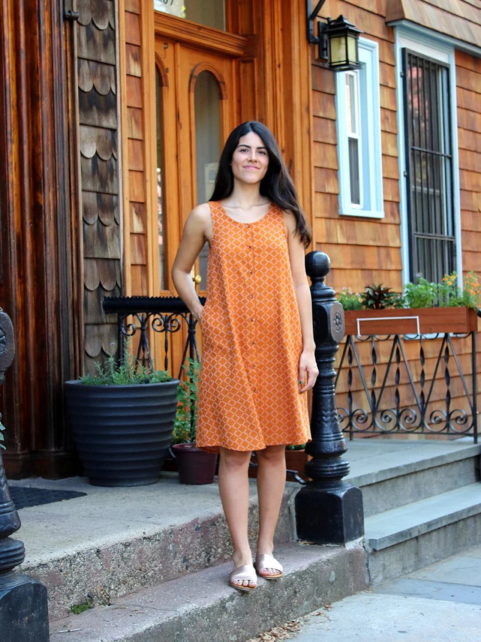 Woman in an orange dress standing on a wooden porch.