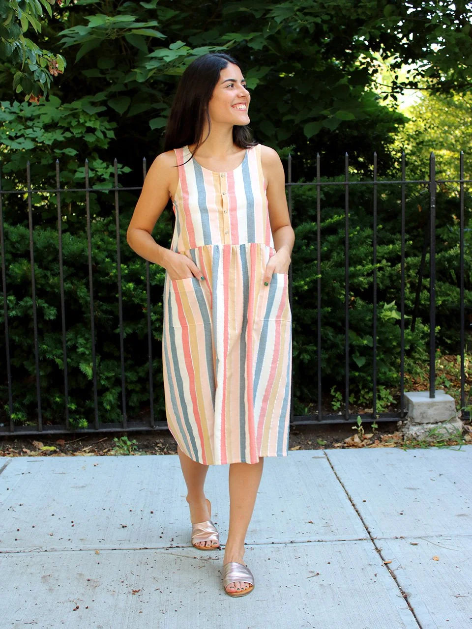 Woman wearing a striped dress standing on a sidewalk with greenery in the background