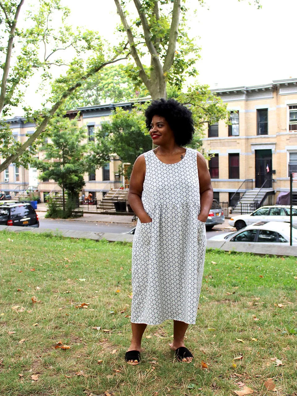 Woman in a white dress with black patterns standing in an urban park.