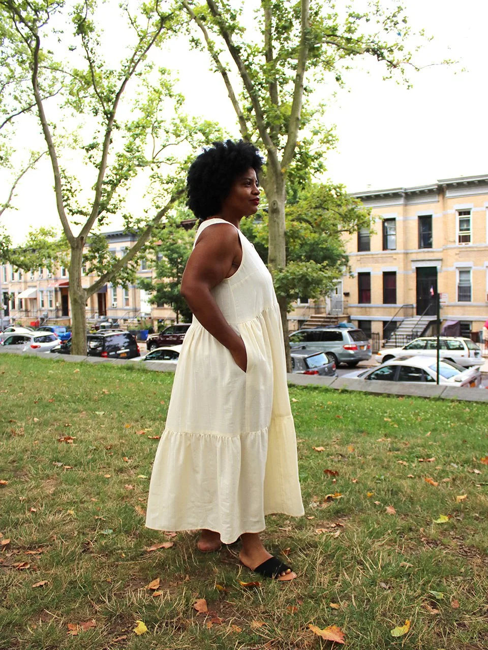 Woman in a white dress standing in a park with trees and buildings in the background