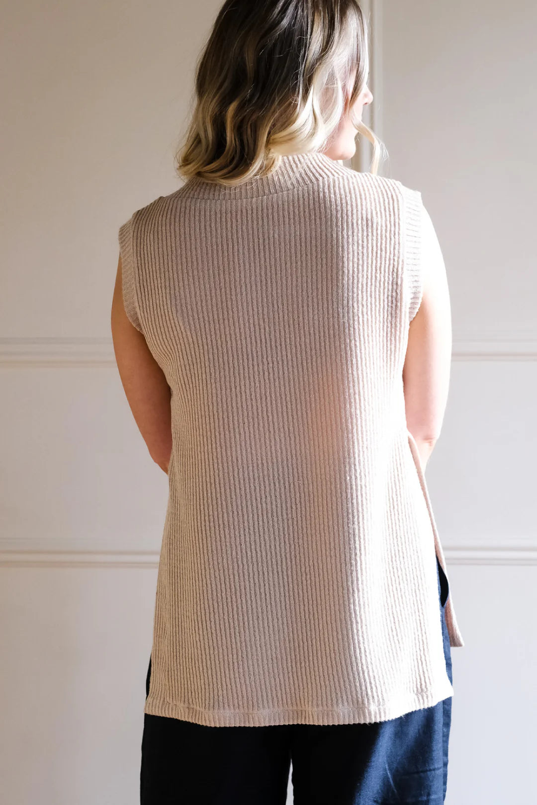 Person wearing a beige ribbed sleeveless sweater against a neutral background