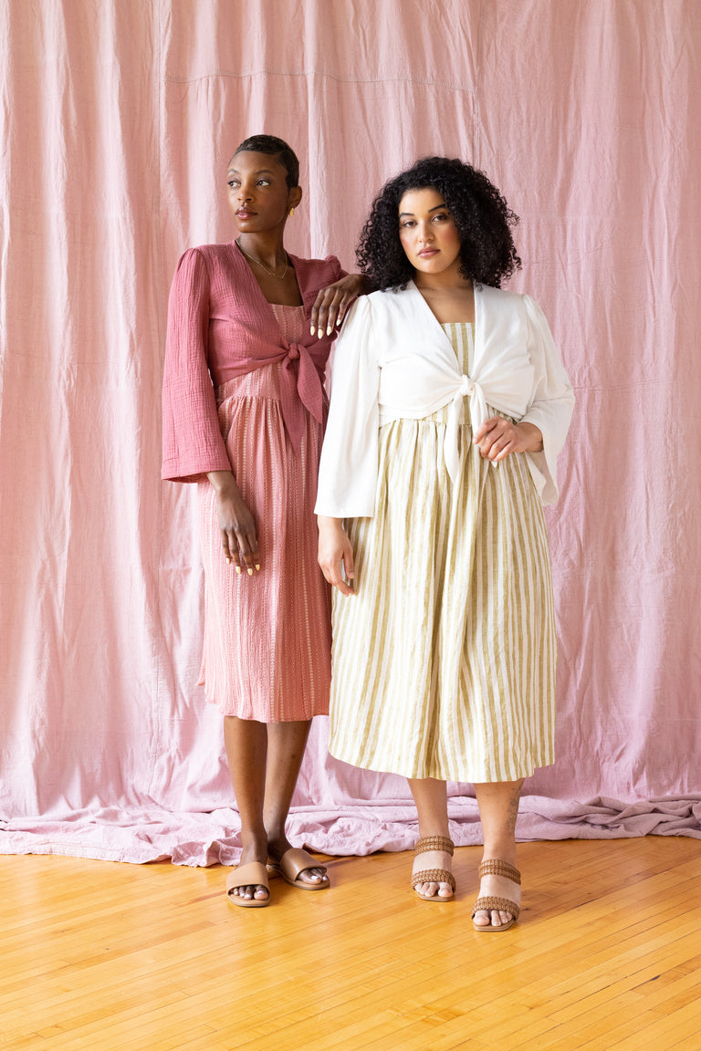 Two models wearing tie-front crop tops, one in a solid pink color and the other in a striped pattern, standing in a room with pink background.