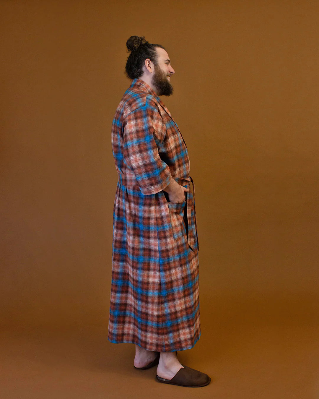 Side full picture of a person in a flannel plaid bath robe against a pumpkin colored backdrop