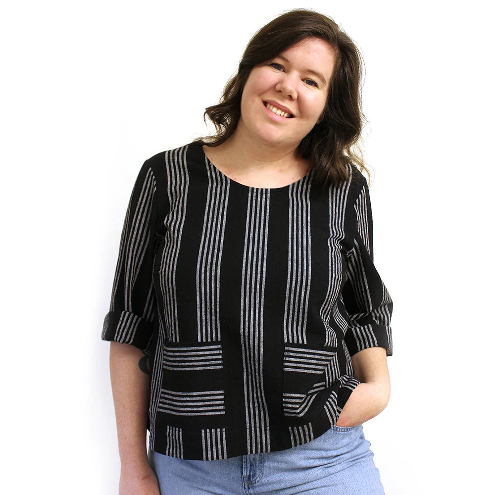 A woman wearing a long sleeved black and white striped top with three quarter, cuffed sleeves.