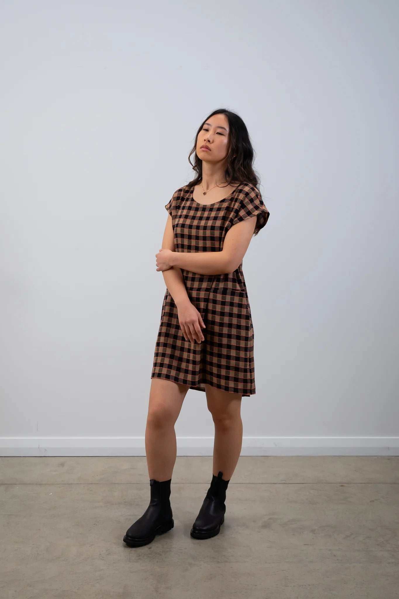 Woman wearing a brown and black checkered dress against a white wall.