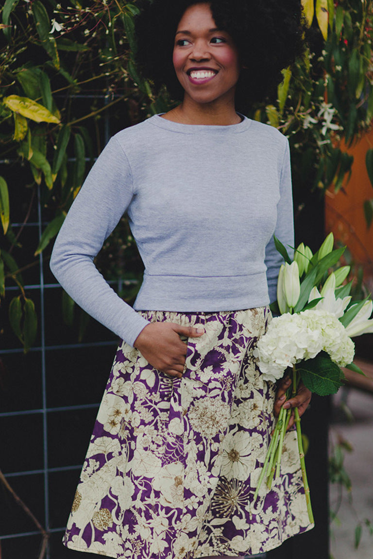 view of model wearing a midi skirt with pockets in a cream and purple floral print and a cropped light blue sweater