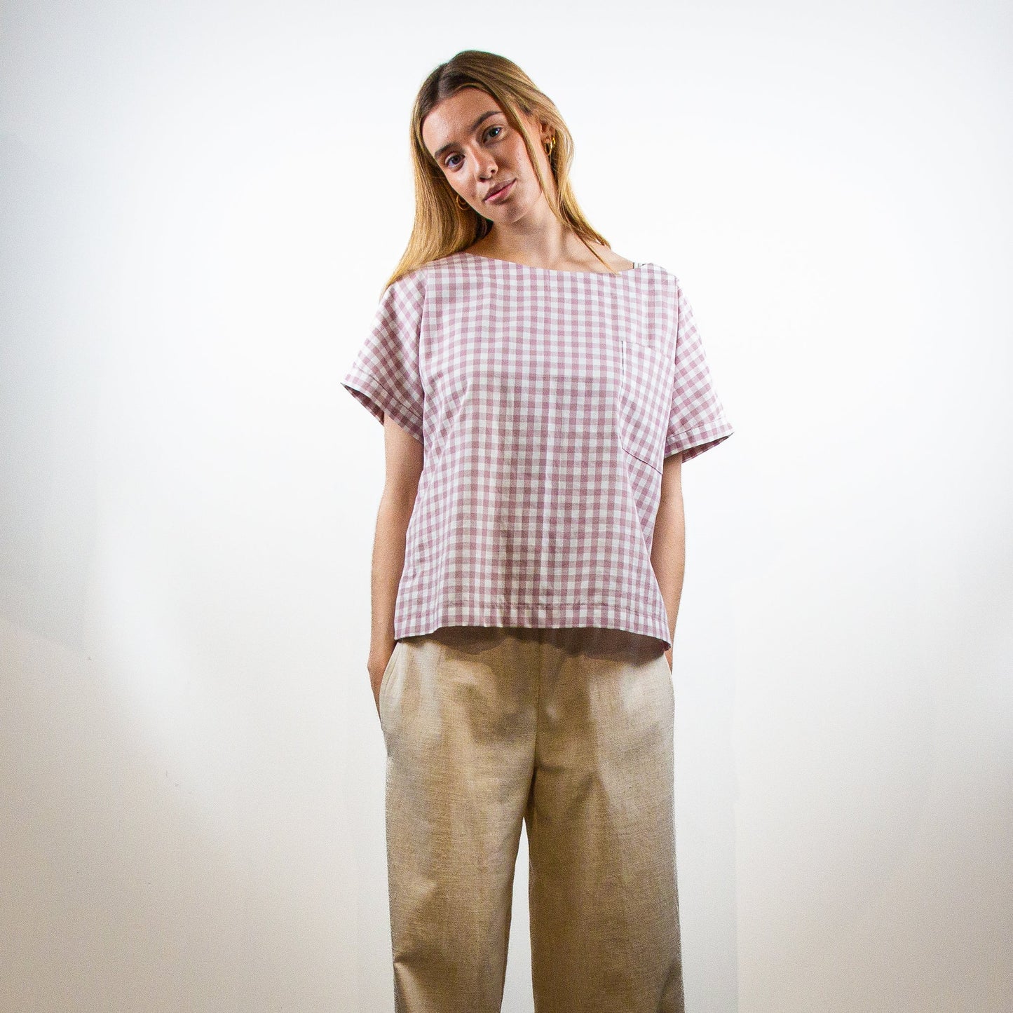 Woman wearing a checkered shirt and beige pants against a white background