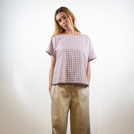 Woman wearing a checkered shirt and beige pants against a white background