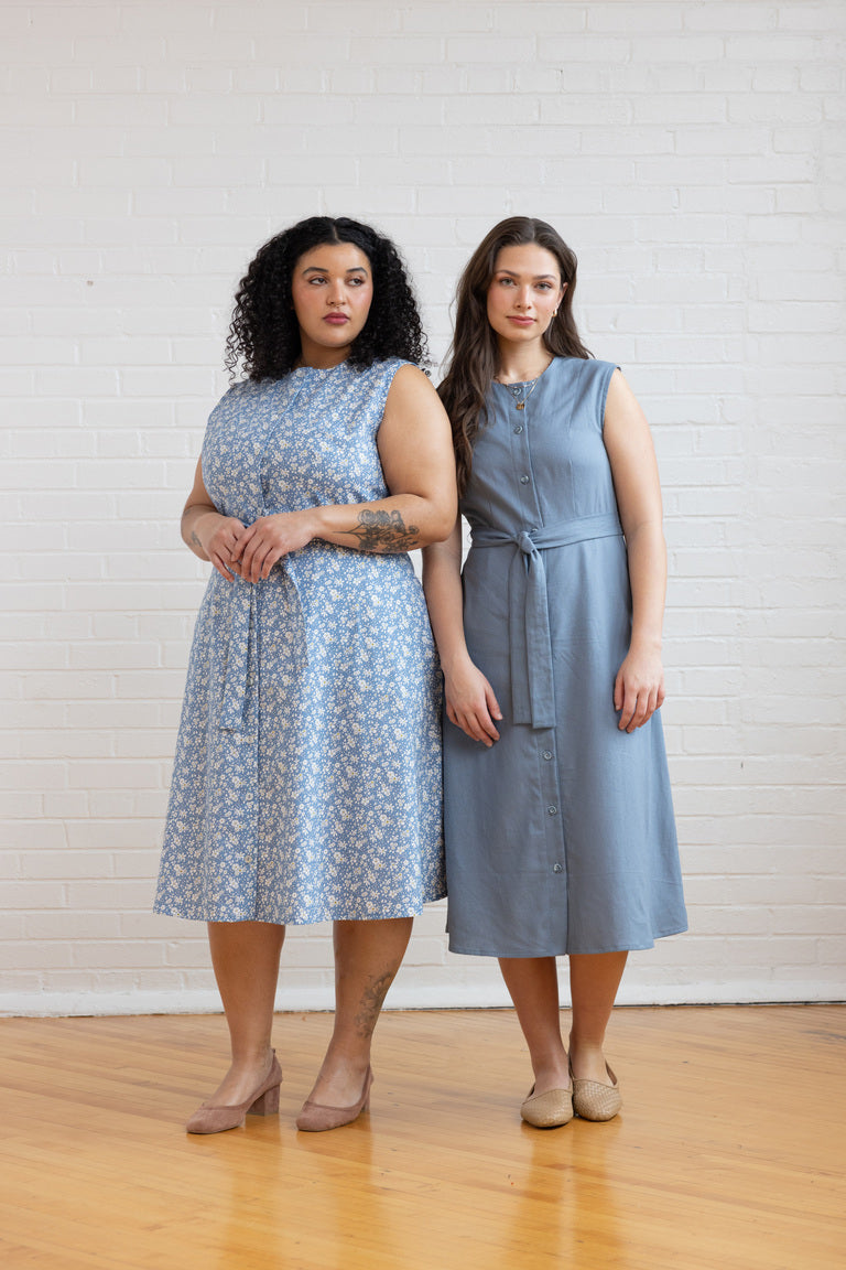 Two women wearing sleeveless dresses standing against a white wall.