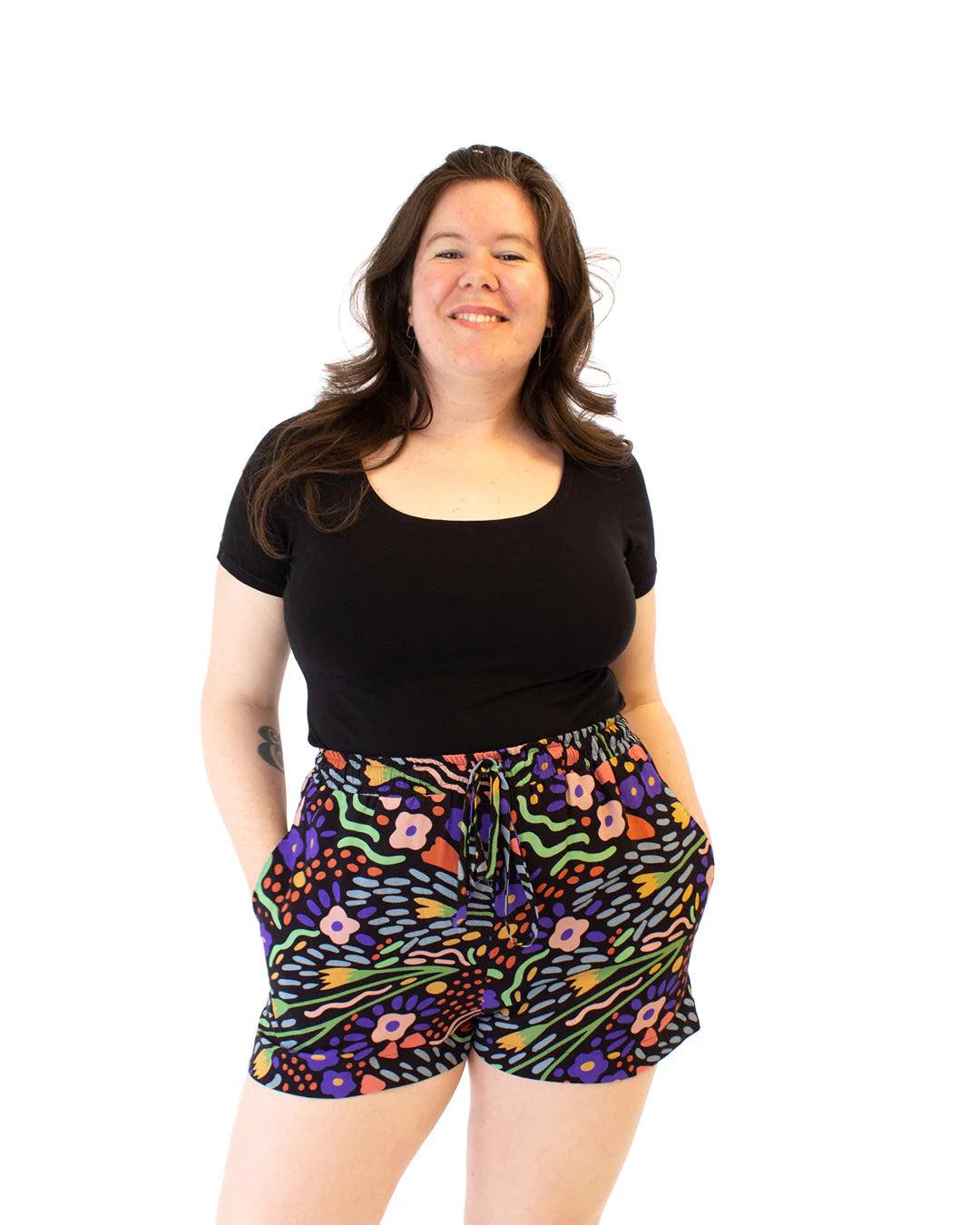 Woman wearing a black top and colorful patterned shorts on a white background