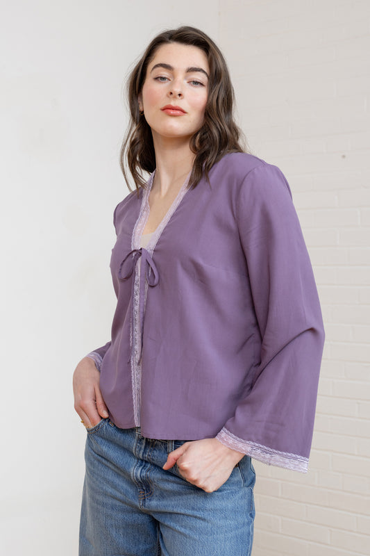 Woman wearing a purple blouse with lace trim against a white background