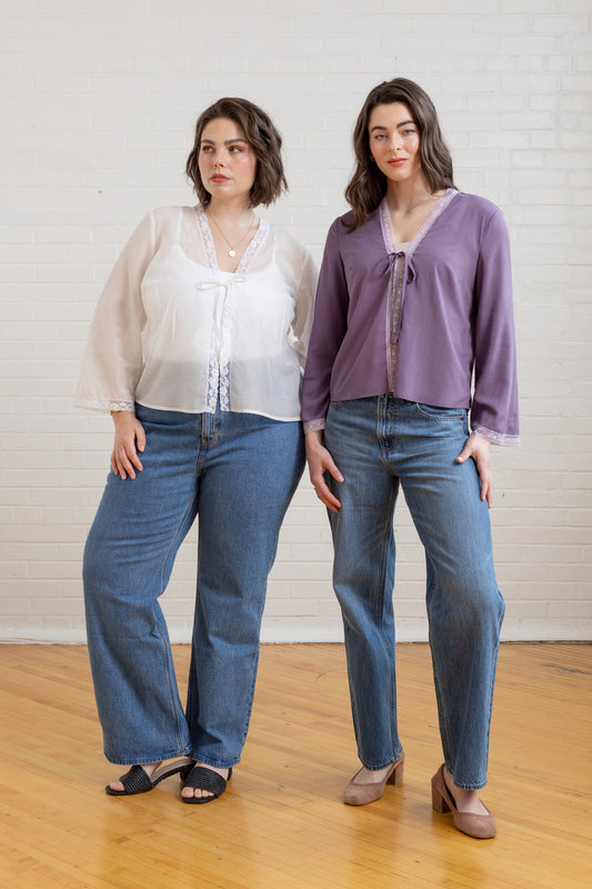 Two women wearing matching outfits of purple shirts and blue jeans against a white brick wall.