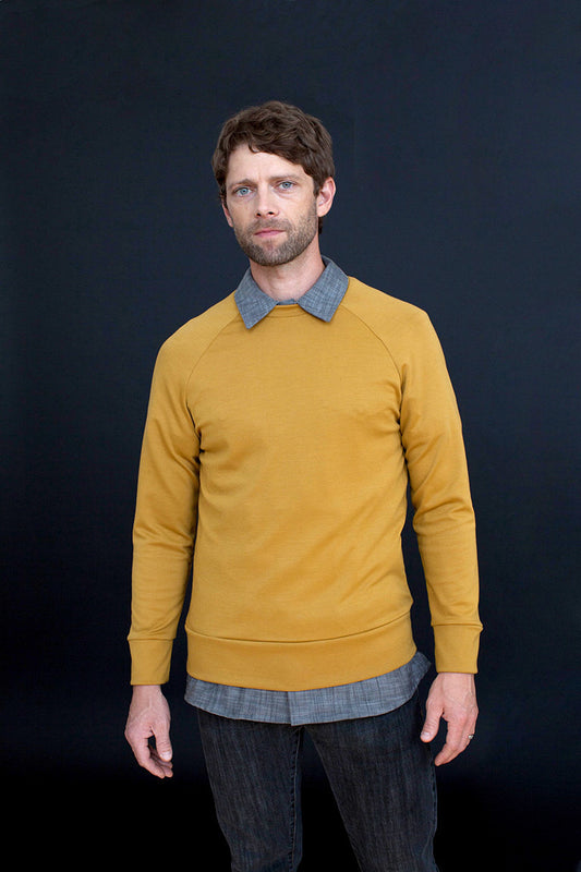 Man wearing a mustard yellow sweater over a plaid shirt against a black background