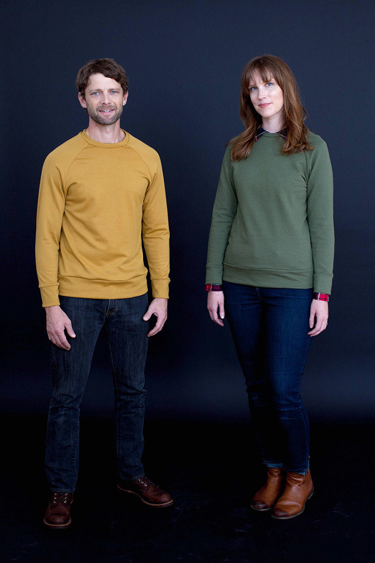 Two people wearing mustard yellow and green sweaters against a dark background