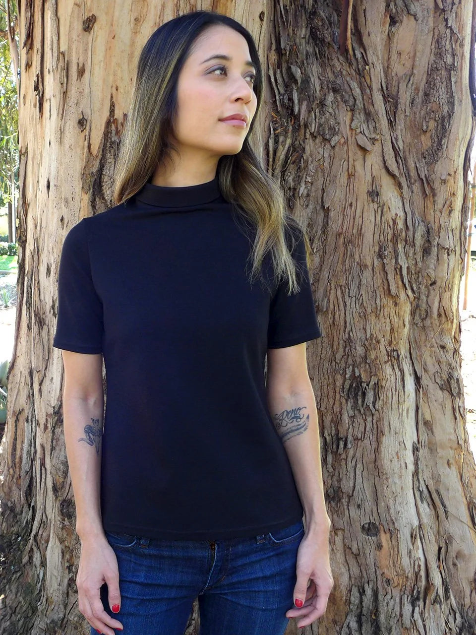 woman with black T-shirt, standing next to a big tree.