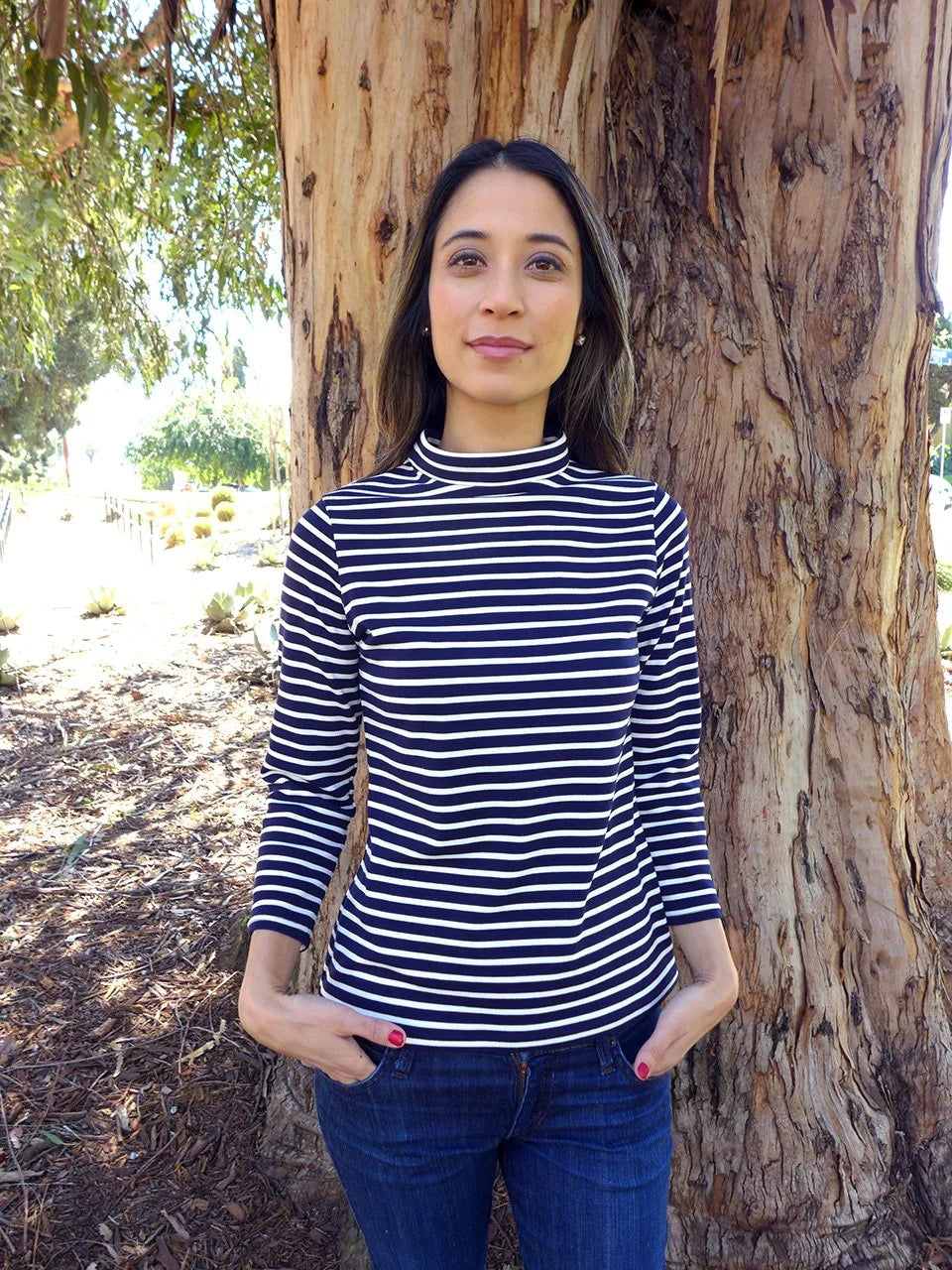 woman with striped T-shirt, standing next to a big tree.