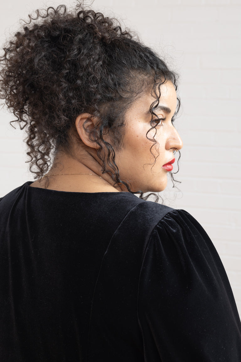 Woman with curly hair wearing a black top against a plain background