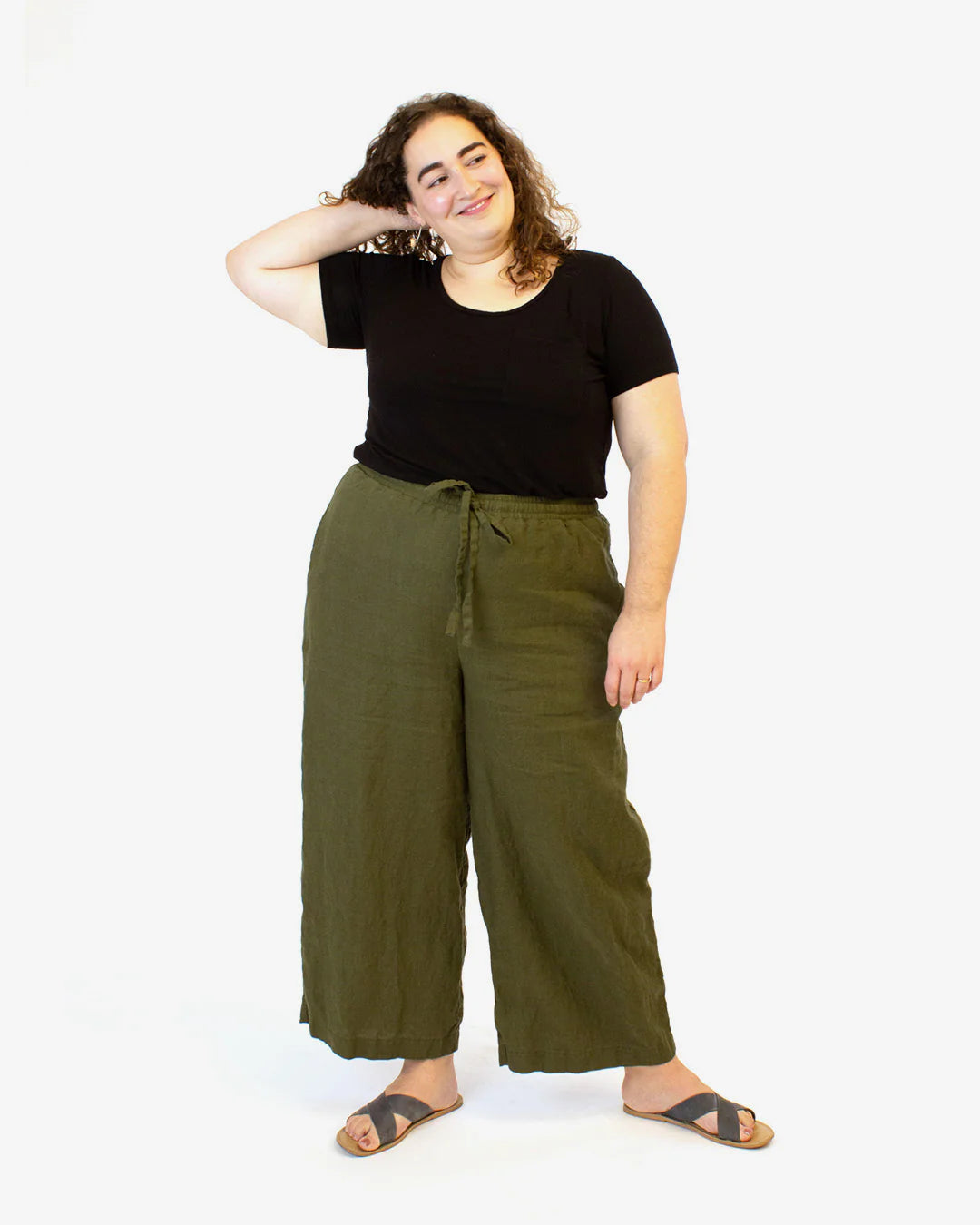 Woman wearing a black top and green wide-leg pants on a white background